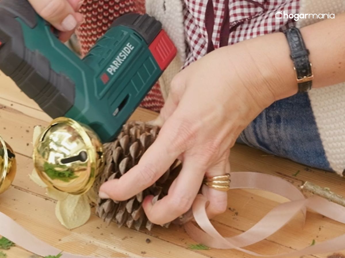 Grapa las cintas de las piñas y añade los detalles dorados para darle luz y un acabado festivo a la corona.