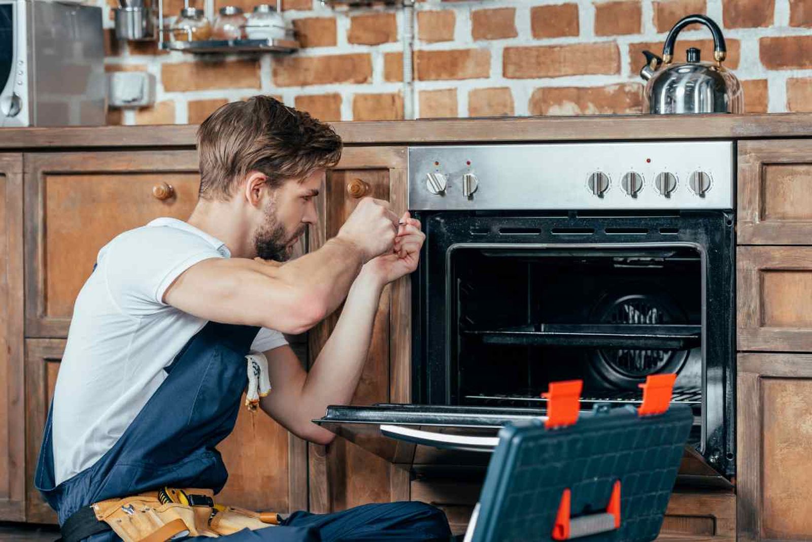 Un técnico repara un horno tras avería eléctrica, algo que podría estar cubierto por tu seguro del hogar.