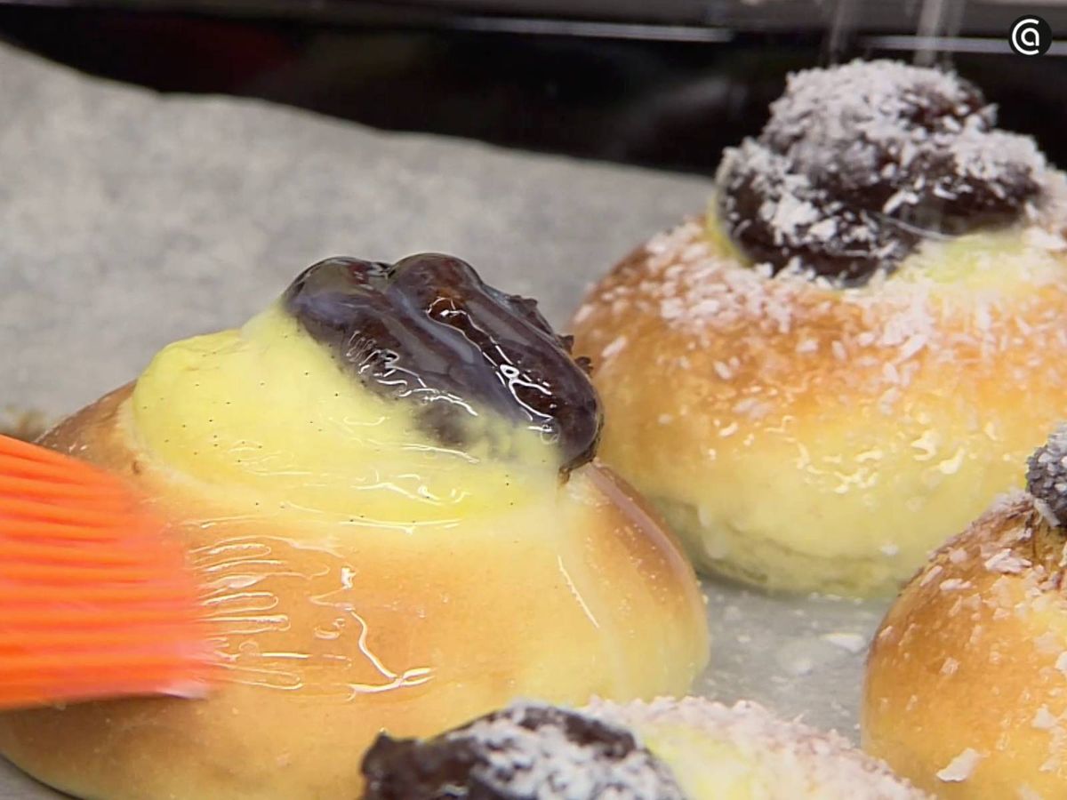 Unta los skoleboller con el glaseado y espolvorea coco rallado